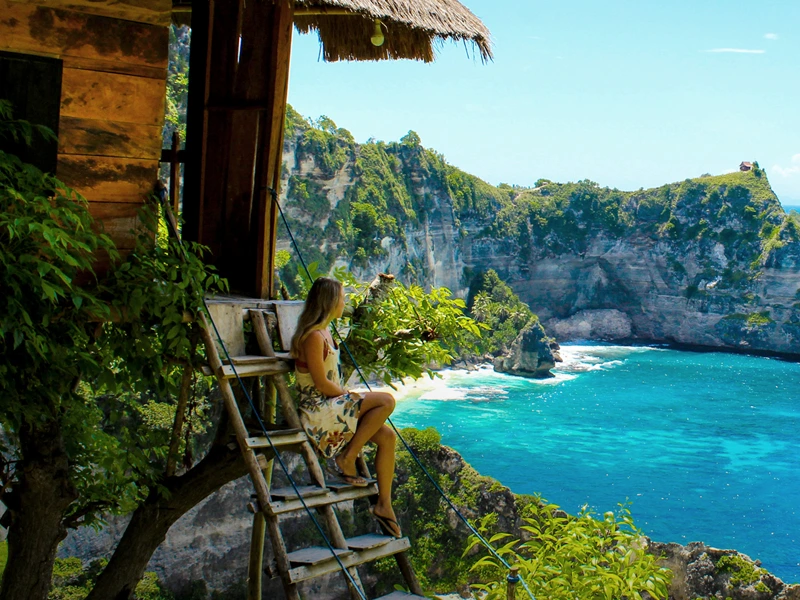 Frau auf der Treppe der Unterkunft mit Blick über eine Bucht auf Bali