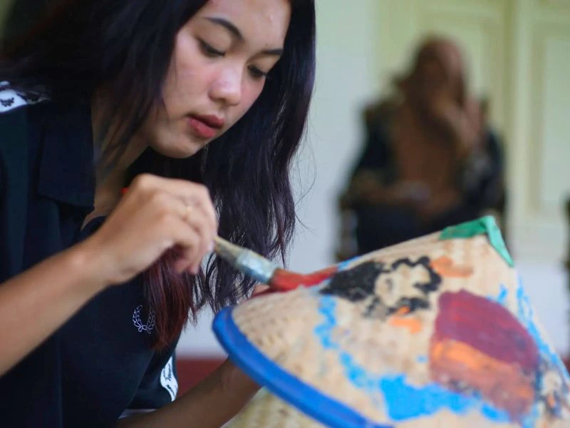 Mädchen bemalt Hut mit Batik bei einem Workshop in Indonesien