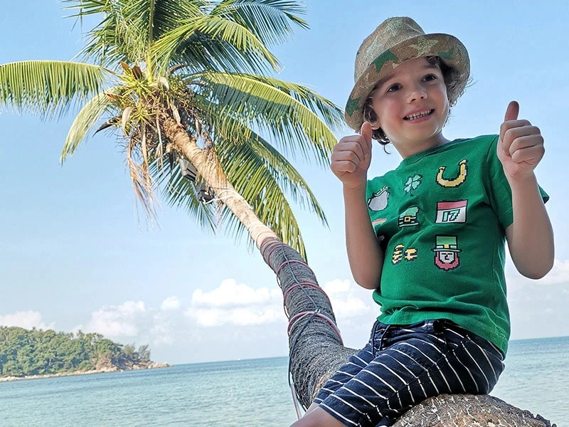 Kind sitzt auf einer Palme am Strand in Thailand