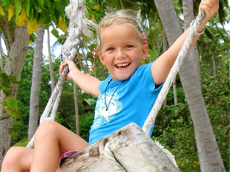 Mädchen auf Schaukel unter Palmen