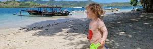 Kind mit Schaufel am Strand mit Boot im Hintergrund