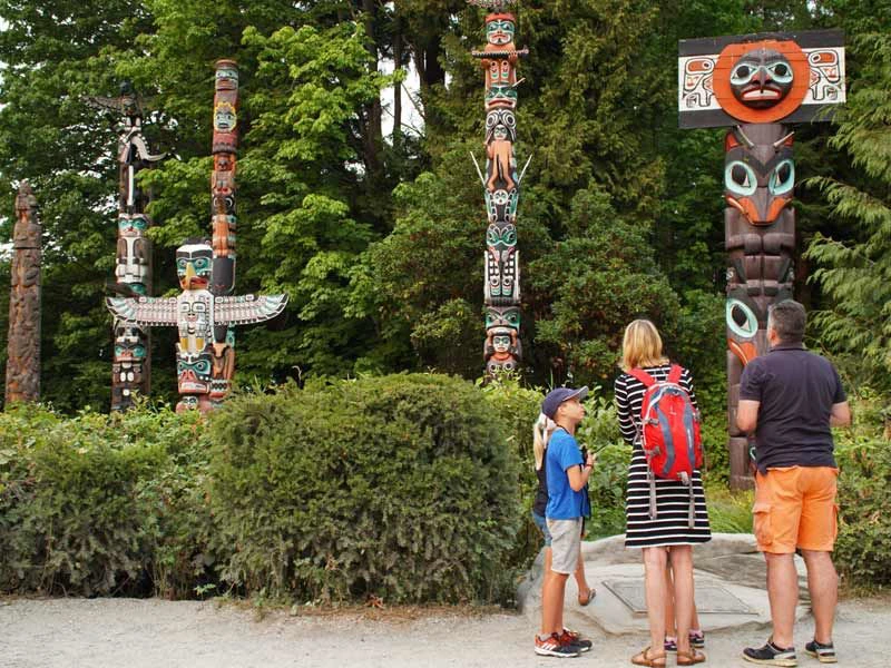 Familie schaut sich die Totem-Pfähle im Stanley Park in Kanada an