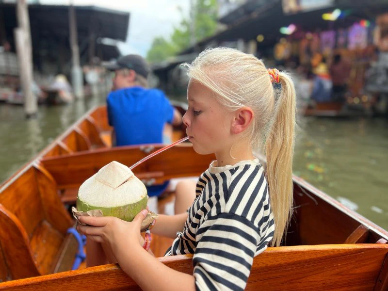 Kind im Boot trinkt mit Strohhalm aus einer Kokosnuss