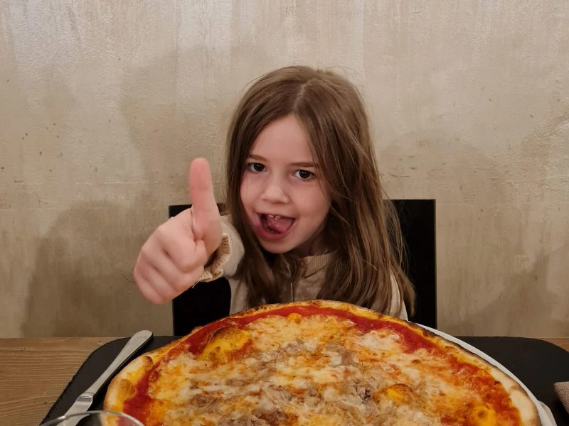 Mädchen mit Daumen hoch sitzt vor einer Pizza