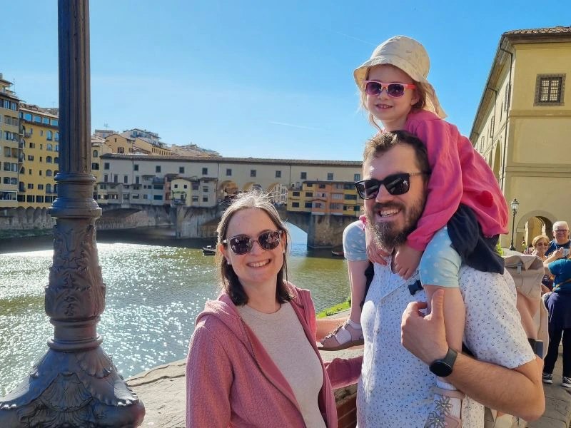 Mutter und Vater mit Kind auf den Schultern vor einer Brücke in Florenz
