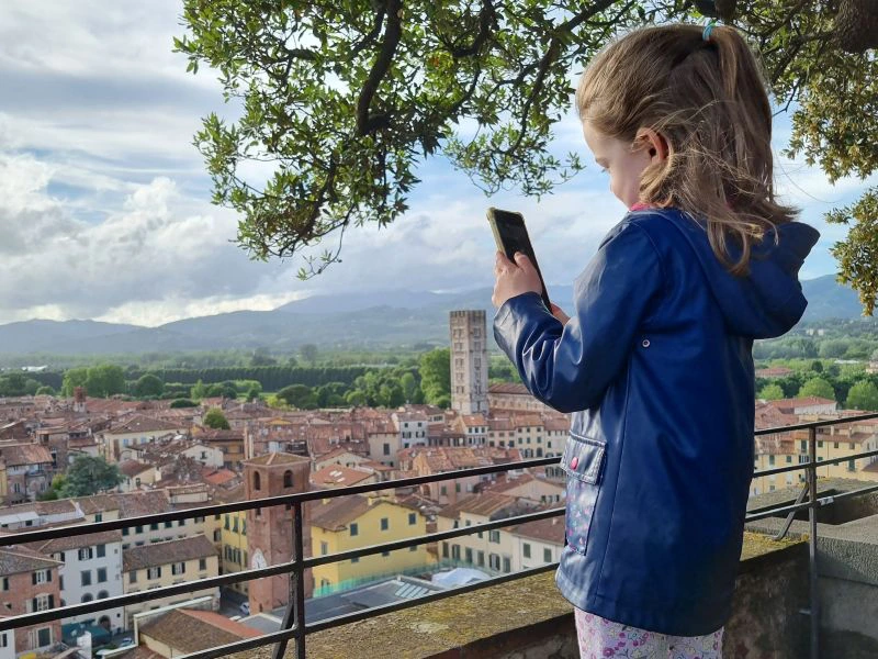 Mädchen steht an einem Zaun, blickt auf Lucca hinunter und macht ein Foto mit dem Handy