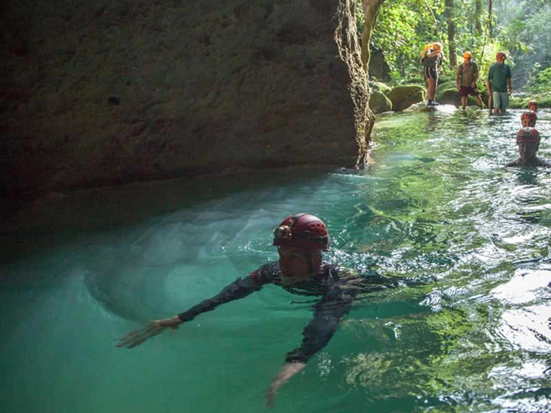 Gruppe mit Helmen schwimmt in eine Höhle.