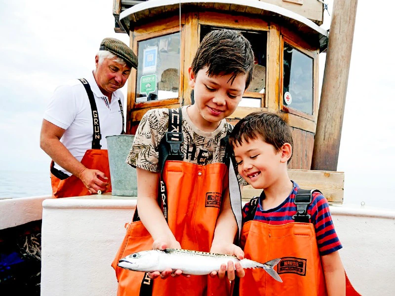 Kinder zeigen ihren Fischfang auf Kutter an der Küsten bei Göteborg, Schweden