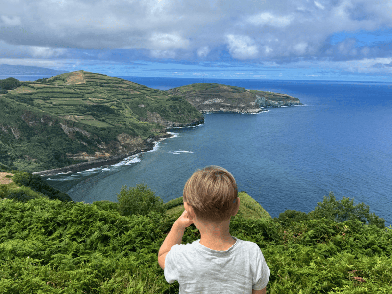 Junge, umgeben von Grün, schaut aufs Meer hinaus