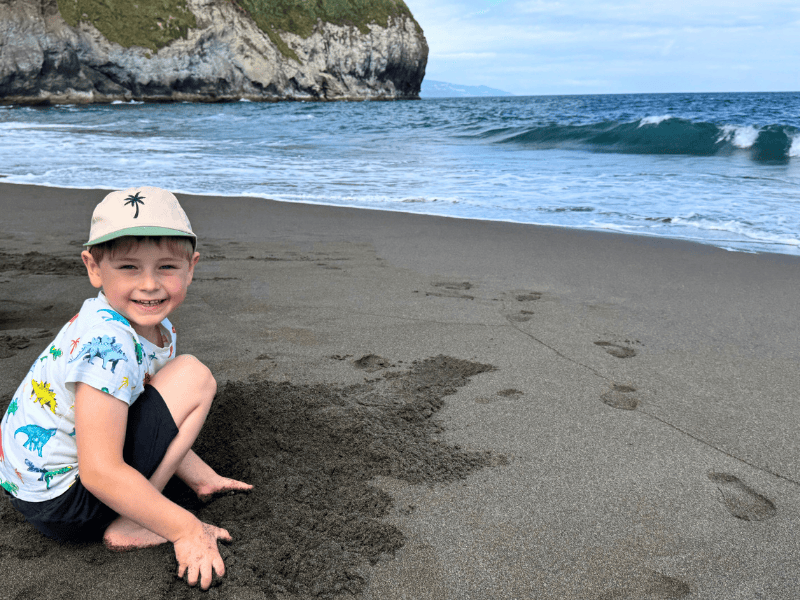 Lächelnder Junge gräbt im schwarzen Sand mit dem Meer im Hintergrund