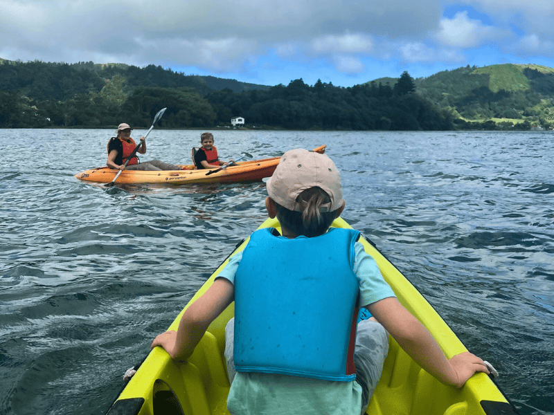 Sohn in gelbem Kajak schaut zu Mutter und Bruder in einem orangenem Kajak, alle tragen Schwimmwesten