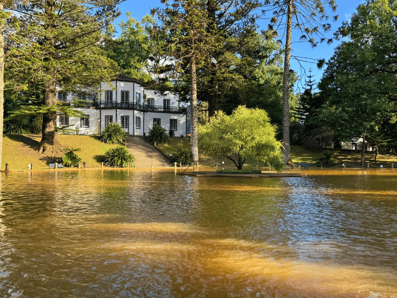 Helles Gebäude umgeben von Bäumen an einem Teich