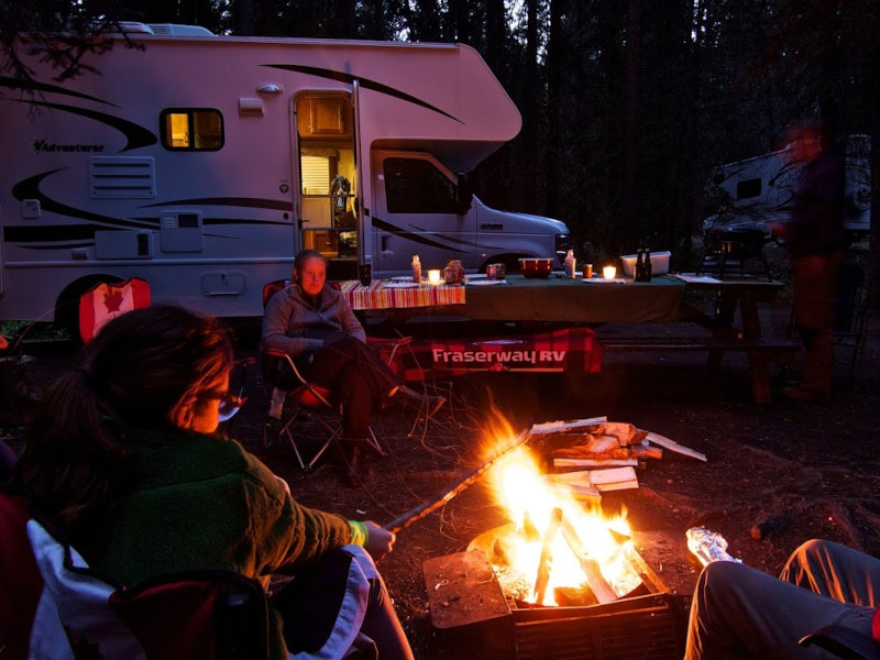 Reisende sitzen am Lagerfeuer neben einem Camper in der Natur