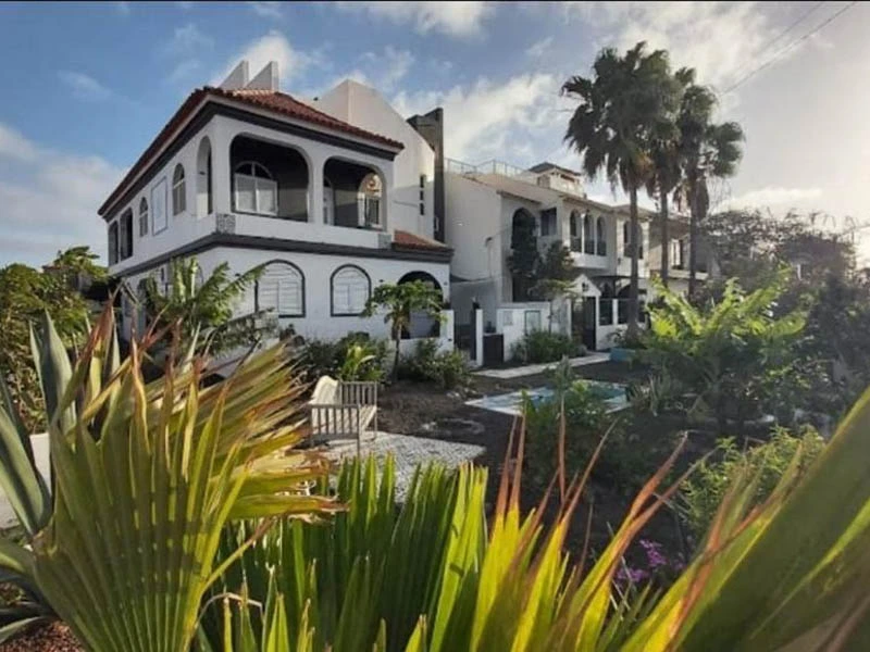 Hotel in Tarrafal mit mediterrane Architektur mit Bögen, Balkonen und einem Turm. Es ist von üppiger, grüner Vegetation umgeben