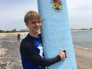 Junge mit Surfbrett am Strand in Sri Lanka