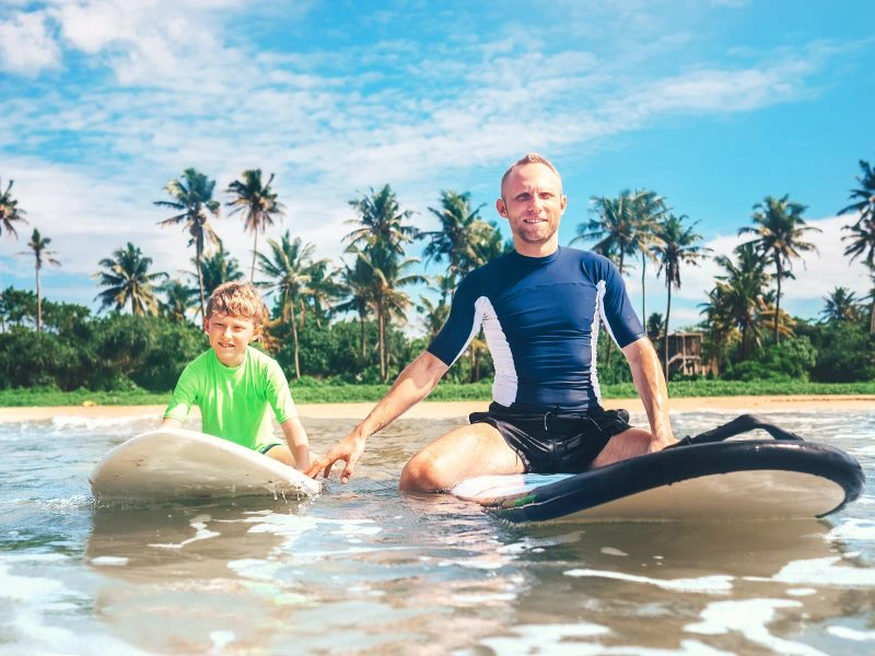 Vater und Sohn sitzen auf einem Surfbrett im Meer in Sri Lanka