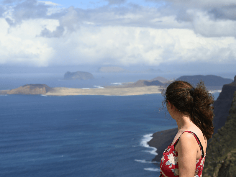 Frau schaut aufs Meer und La Graciosa, der Himmel ist voller Wolken