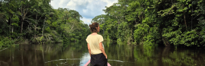 Frau, stehend, im Kanu auf Fluss, umgeben von grüner Vegetation