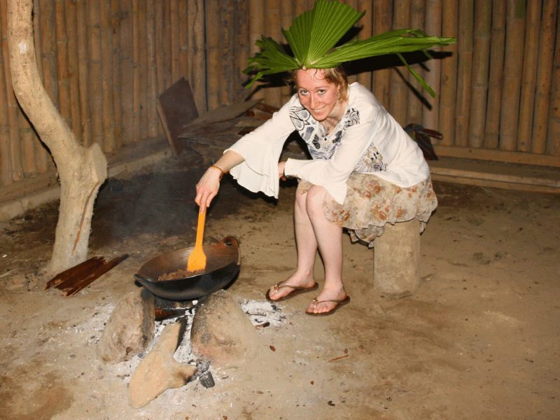Touristin mit grünem Blätter Haarschmuck röstet Kakaobohnen auf einem Feuer