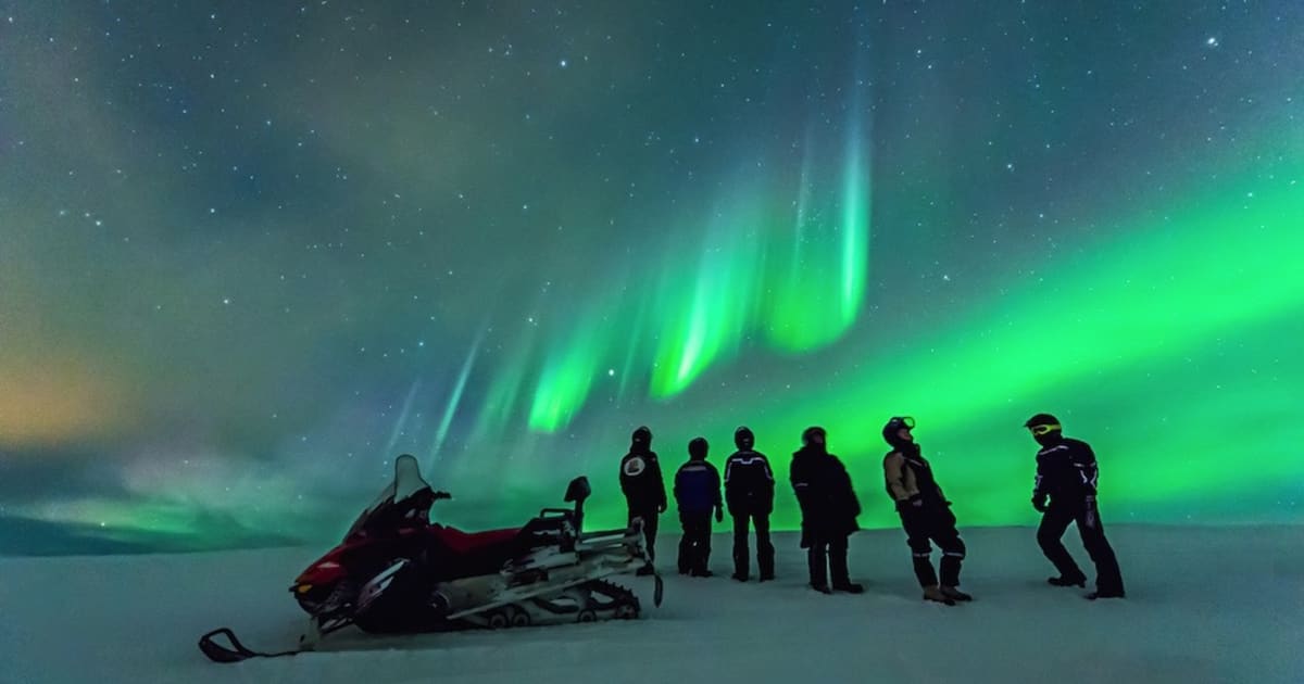 Reisende bei Schneemobiltour am Abend unter Nordlichtern in Lappland