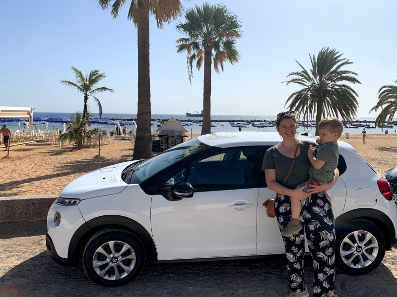 Frau mit Kind vor Mietauto an der Küste in Teneriffa, Spanien