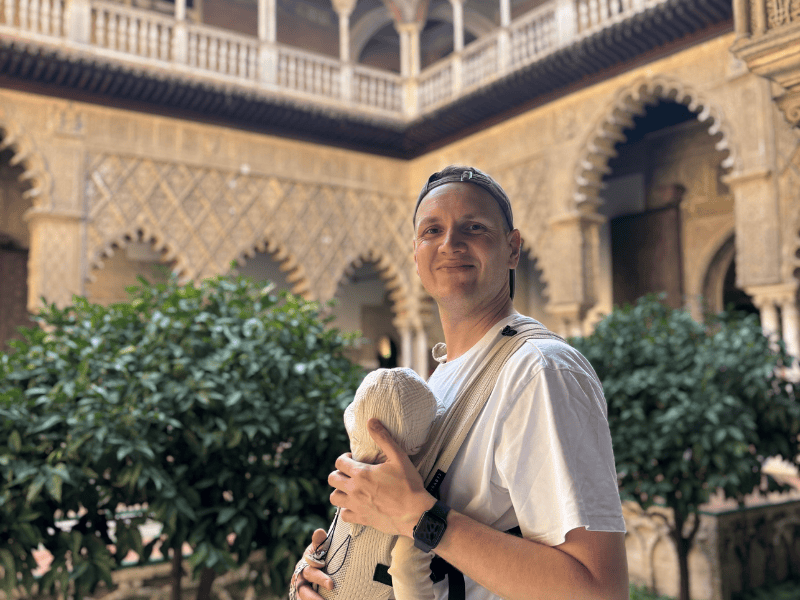 Mann mit Baby in der Trage in einem prächtigen Innenhof in Sevilla, Spanien